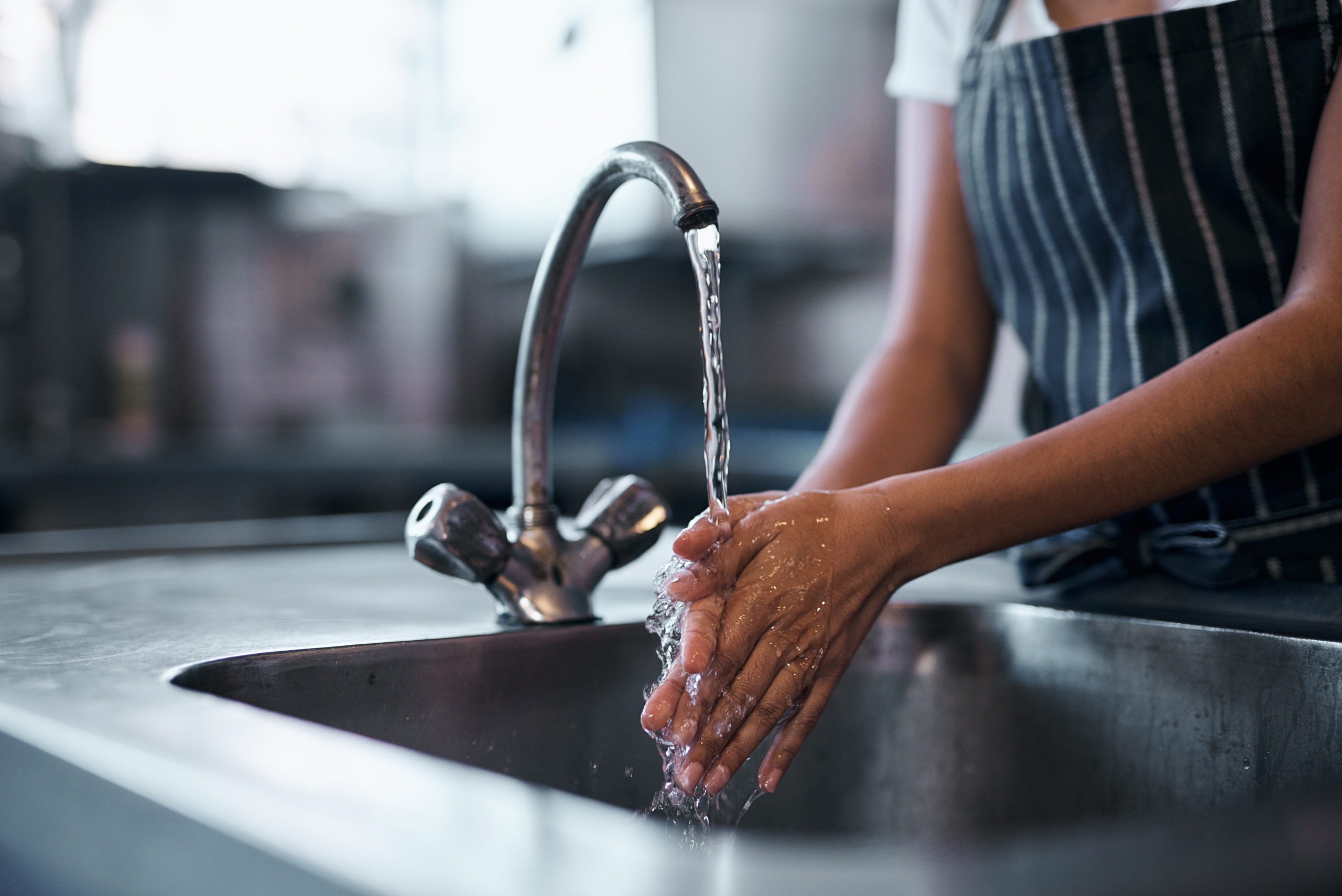 Kvinna som tvättar händerna i en kökskran med rent vatten renat med ett vattenfilter