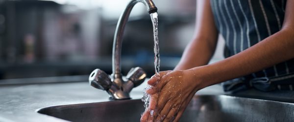 Kvinna som tvättar händerna i en kökskran med rent vatten renat med ett vattenfilter